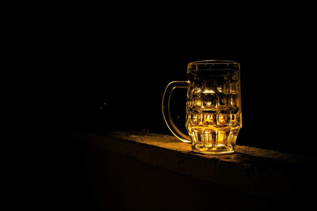 A glass beer mug illuminated against a dark background, creating a moody atmosphere.